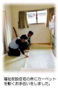 福祉仮設住宅の床にカーペットを敷くお手伝いをする支援員