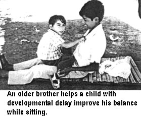 An older brother helps a child with developmental delay improve his balance while sitting.