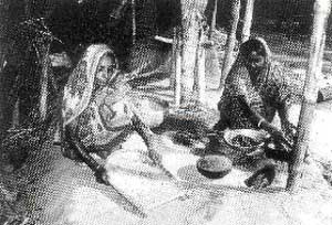 写真1：民族衣装姿の女性2人が床に座って精米作業をしている様子。