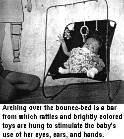 Arching over the bounce-bed is a bar from which rattles and brightly colored toys are hung to stimulate the baby's use of her eyes, ears, and hands.