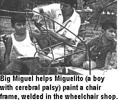Big Miguel helps Miguelito (a boy with cerebral palsy) paint a chair frame, welded in the wheelchair shop.