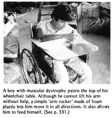 A boy with muscular dystrophy paints the top of his wheelchair table.