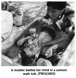 A mother bathes her child in a cement wash tub.