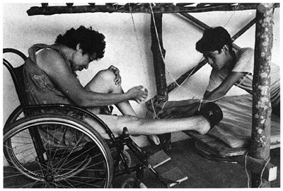 A man who is sitting in wheelchair works with other's help.