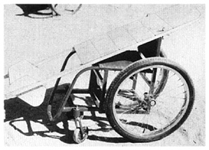 Non-folding steel tube wheelchair frame with a wooden lying board mounted on top.
