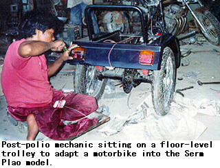 Post-polio mechanic sitting on a floor-level trolley to adapt a motorbike into the Serm Plao model.