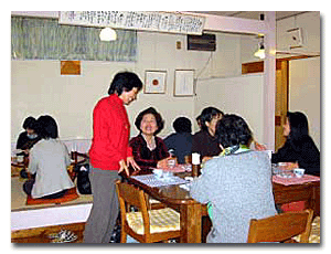 photo of Sachiko Matsuura visiting at a table with several diners during a meal