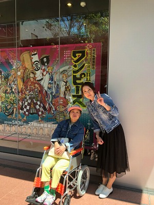 劇場前で車いすに座っているマリさんとのツーショット写真