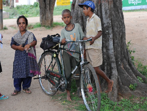 障害のあるCBRワーカーの女性。カバンを持ちにくいため、地元の子どもたちが自転車で運んであげている。