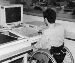 車椅子の障害者がコンピュータに向かって仕事をしている写真