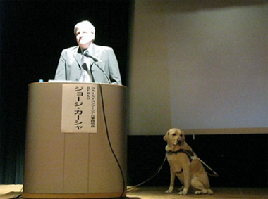 講演を行うジョージ・カーシャー氏と盲導犬・マイキーの写真