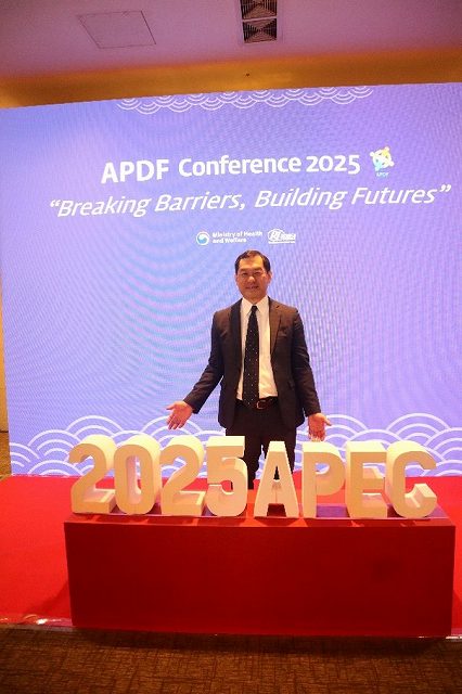「APDF Conference 2025」および「2025 APEC」と書かれた会場入口の看板の前に立つ村上氏