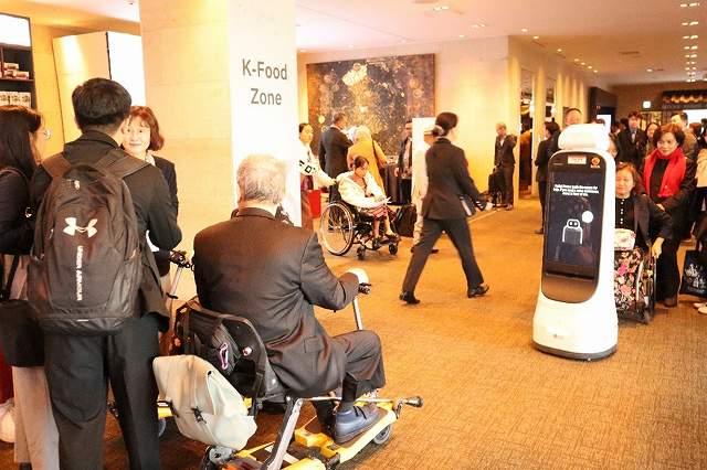 会議場ロビーの様子。車いすユーザー等の参加者が行き交う中、自律走行する案内ロボットが稼働している