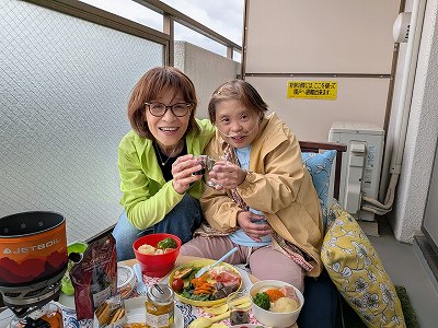 ベランダで友達の英子さんとランチをしながら、乾杯をして笑顔を見せる真理さん