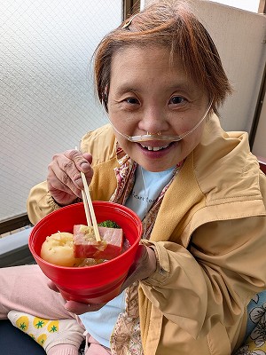 ベランダで、赤い器に入ったポトフのお肉をお箸で持ち上げて嬉しそうな真理さん