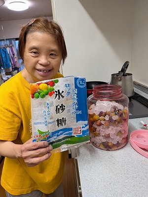 梅が入った瓶の横で、氷砂糖の袋を手に持って笑顔を見せる真理さん