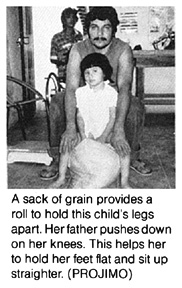  A sack of grain provides a roll to hold this child's legs apart. Her father pushes down on her knees. This helps her to hold her feet flat and sit up straighter. (PROJIMO)