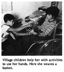 Village children help her with activities to use her hands. Here she weaves a basket.